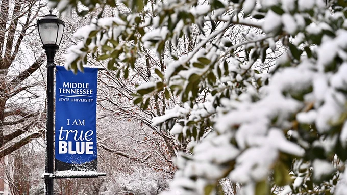 One of MTSU’s “True Blue” banners hangs from a lamppost amid snow-covered tree branches and leaves between Peck Hall and Kirksey Old Main today, Feb. 7. (MTSU photo by J. Intintoli)