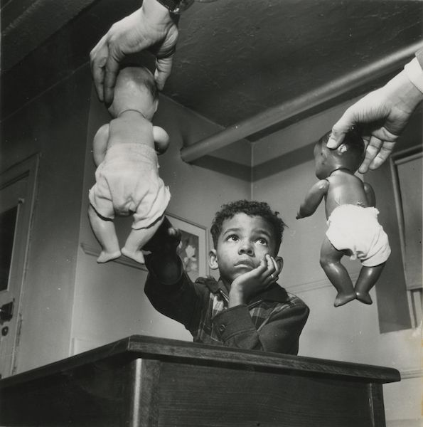 black and white photo of a young African American boy being showed two baby dolls