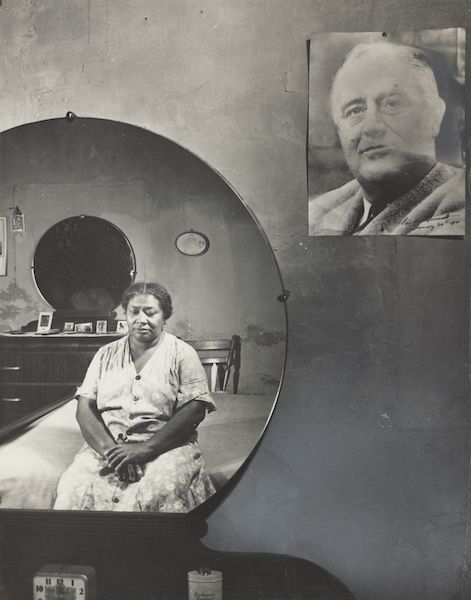 black and white photo of an older African American woman in her bedroom shown reflected in a round mirror