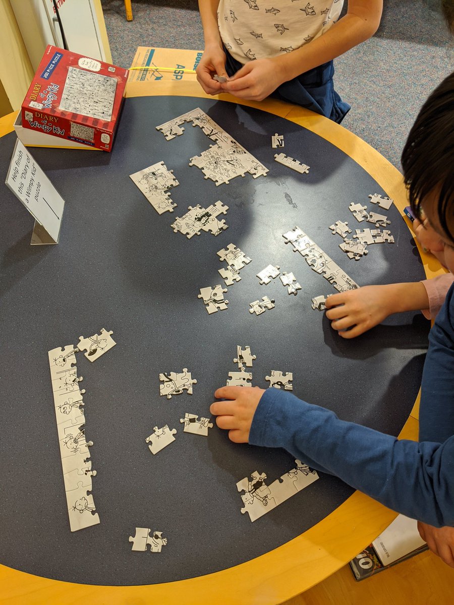 Library patrons working on puzzle of images from the book series "Diary of a Wimpy Kid".