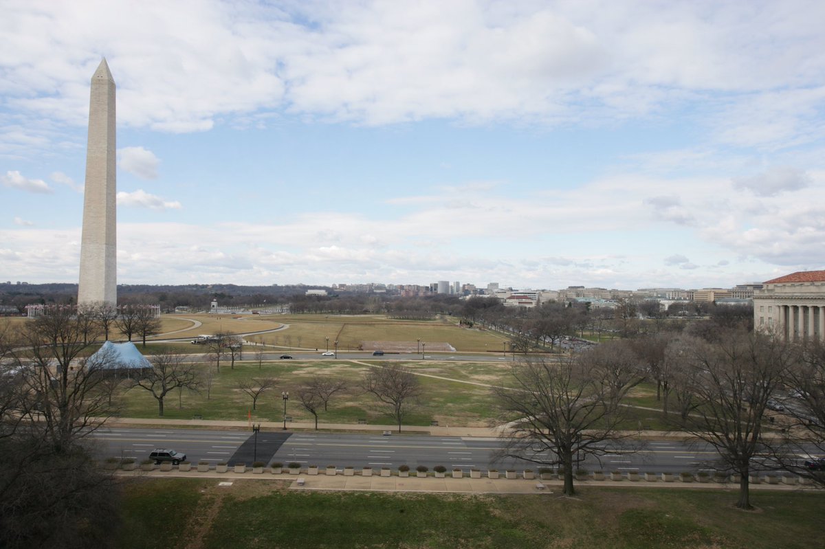 View from a high vantage point of part of the National Mall. On left, Washington Monument. A few trees.