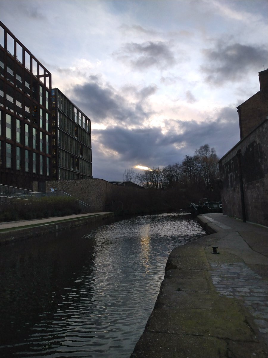 The Regent Canal in London. Although the sun is hidden behind the clouds, you can see a reflection in the water.