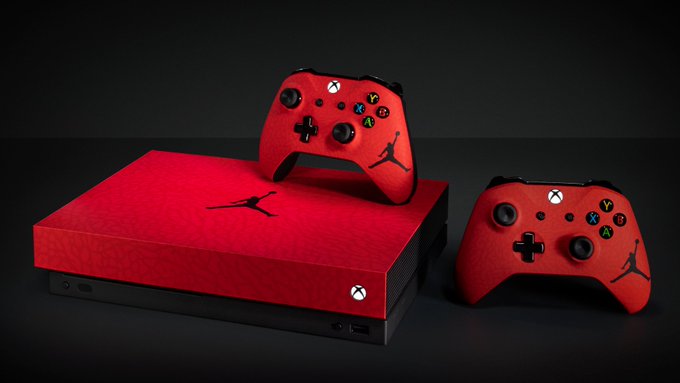 A custom red Limited Edition Nike Jordan Brand Xbox One X and two Xbox One controllers sit on a dark black background.