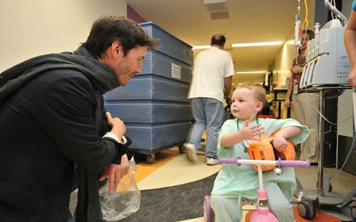 Keanu Reeves kneels down to greet 2-year-old hemophilia patient, Ethan Klamm, at Miller Children's Hospital April 15, 2010