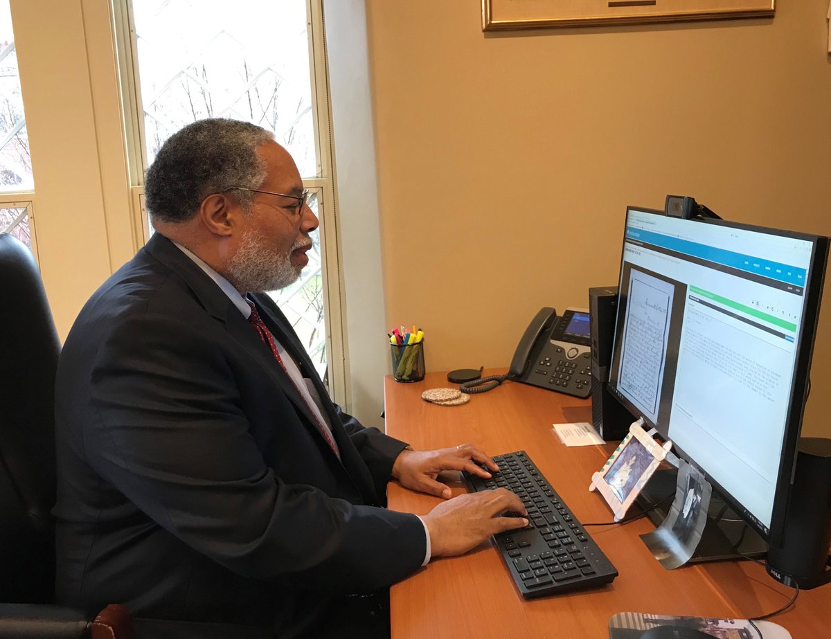 Lonnie G. Bunch III is at his desk looking at a historic document on his computer screen. His hands are on keyboard. He wears his glasses. He is typing.
