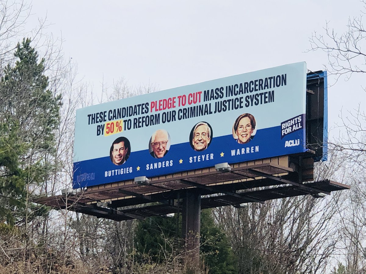billboard on the side a road that reads "These candidates pledge to cut mass incarceration by 50% to reform our criminal justice system" with images of Pete Buttigieg, Bernie Sanders, Tom Steyer, and Elizabeth Warren