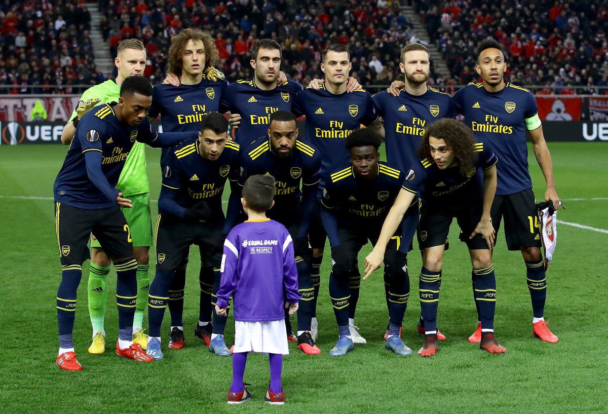 TheArsenalDay's tweet photo. The Arsenal squad invite a young mascot who was still on the pitch in their team photo before kick-off against Olympiakos tonight. ❤️ https://t.co/LWhDzDj1Vw