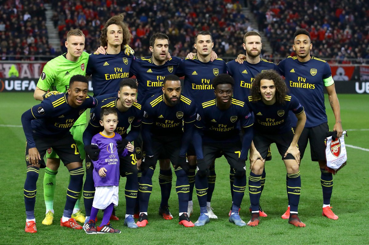 TheArsenalDay's tweet photo. The Arsenal squad invite a young mascot who was still on the pitch in their team photo before kick-off against Olympiakos tonight. ❤️ https://t.co/LWhDzDj1Vw