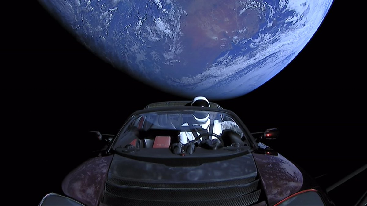 Elon Musk's Tesla Roadster, with Earth in background. "Starman" mannequin wearing SpaceX Spacesuit in driving seat. Camera mounted on external boom.