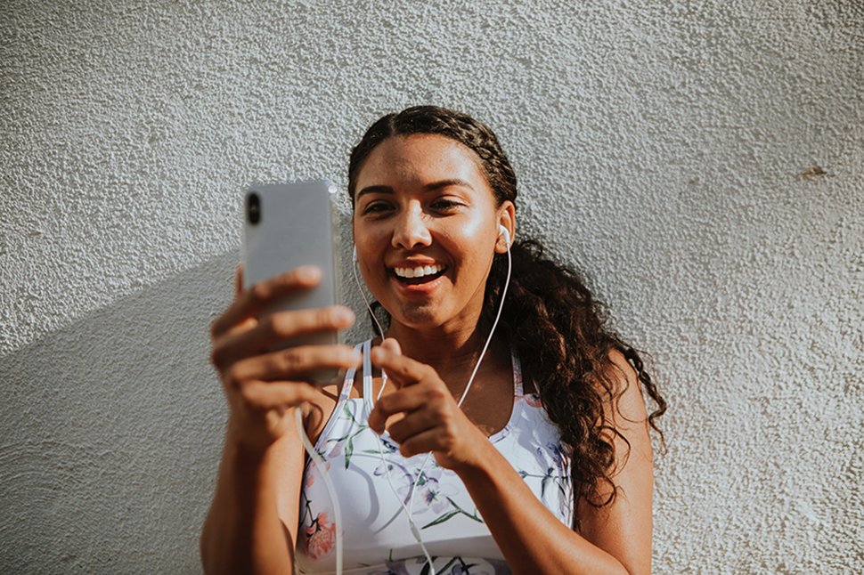 a woman smiling at her smartphone listening to it with headphones