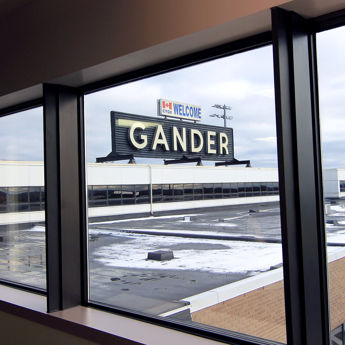 Photo of a Welcome to Gander sign at the Gander Airport through a window