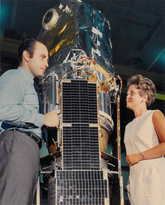 Marjorie Townsend stands in front of a satellite and talks to a man.