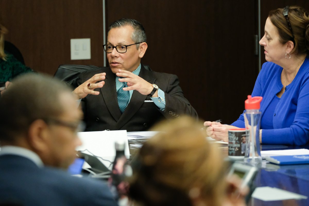 A photo of a man speaking at a table.