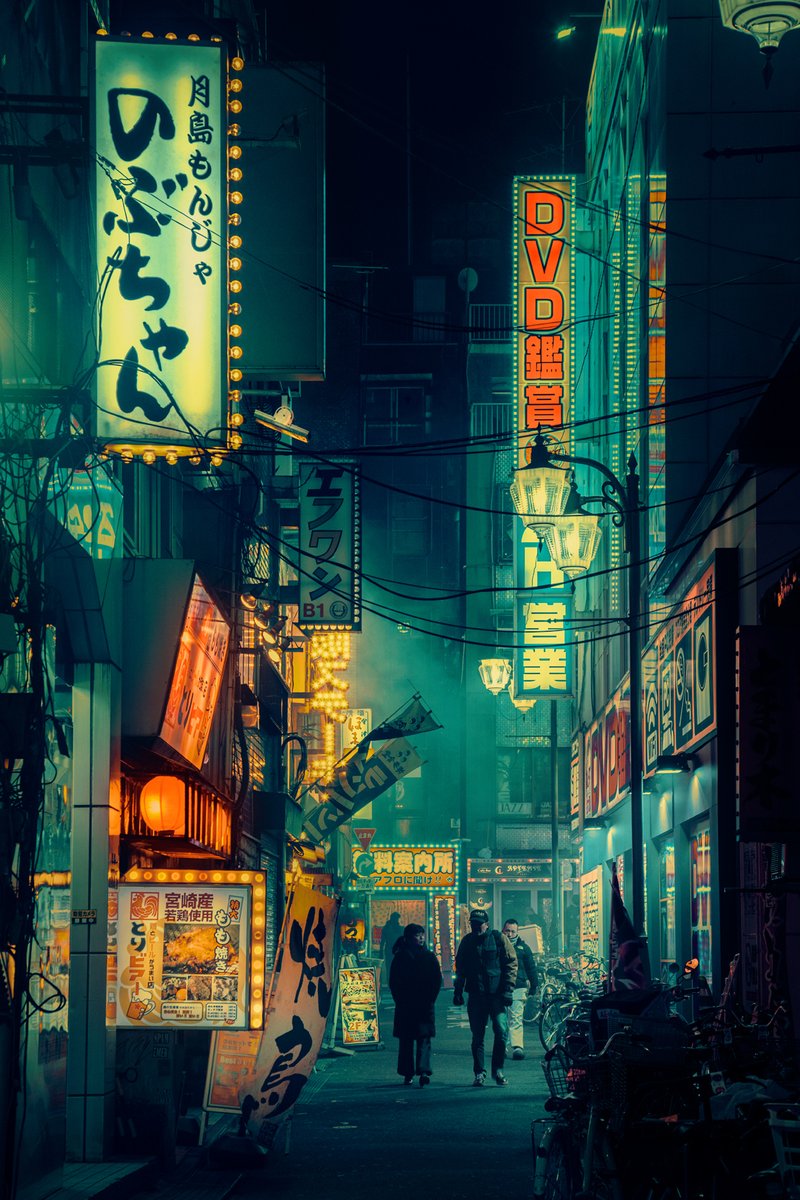 A photograph of Tokyo at night. A couple walking down an alleyway in Tokyo. It is surreal looking and looks like a painting. It is green and orange and yellow in color. Tall signs for restaurants are written in Japanese. One reads DVD. There is smoke from izakayas and wires hang overhead.