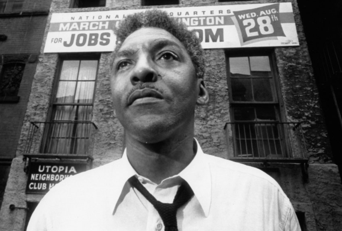 Image of Bayard Rustin. He stands in front of a banner for the March on Washington for Jobs and Freedom.