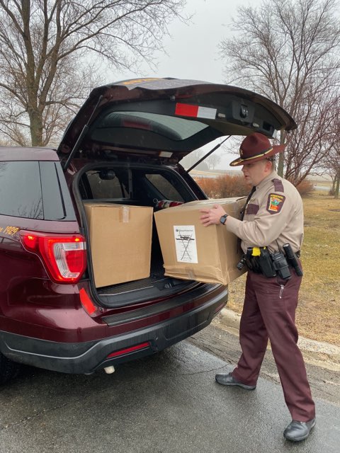 Trooper loads masks into car. 