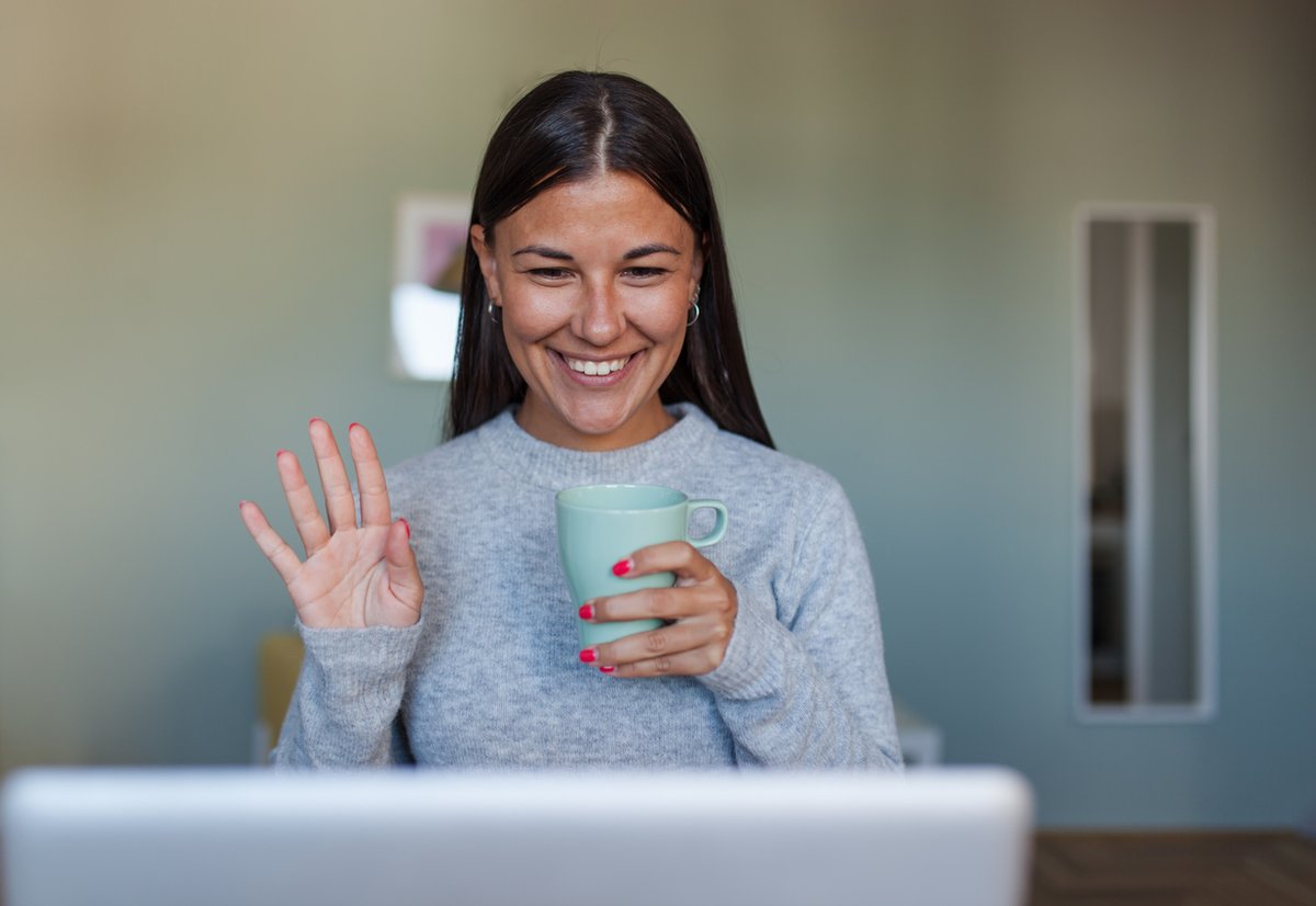 A woman waving at colleagues over video call. 