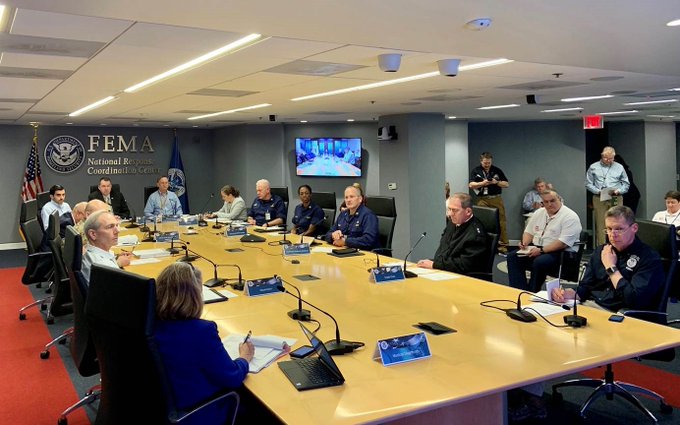 More than a dozen individuals sitting for a meeting around a table.