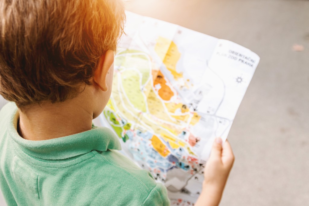 a young boy looking at a map outside in the sunlight