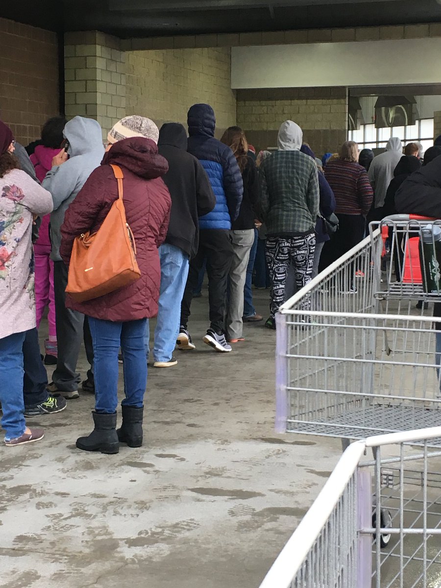 The line outside Costco. Hundreds of shoppers. People are close. It is cold and rainy. 15 minutes until opening.