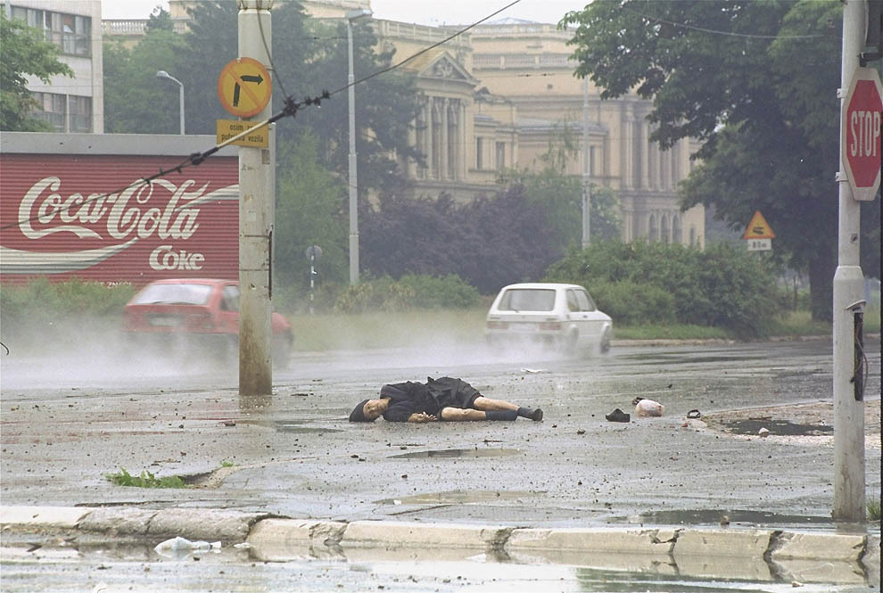 June 11, 1992, a Bosnian woman is shot by a Serb sniper while walking the “sniper alley” area of Sarajevo. Her grocery bag and shoe lay next to her.