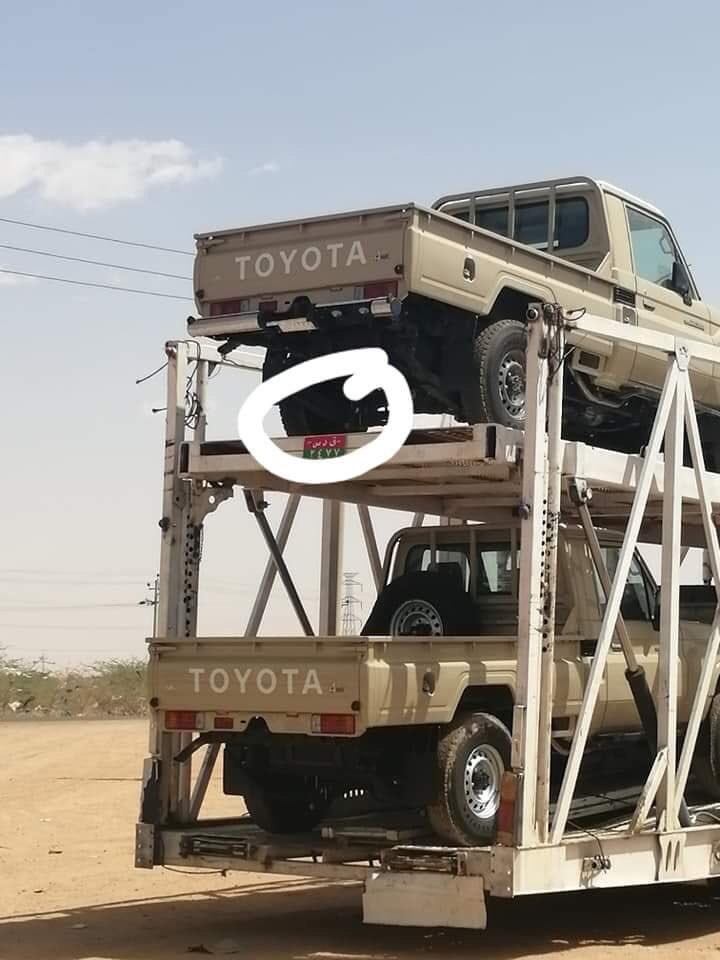 There are photos from early 2019 circulating on Sudanese social media of a vehicle transporter, loaded with beige Toyota Land Cruiser pickup trucks. A close-up shows that one of the transporters has the red and green RSF number plate. 14/