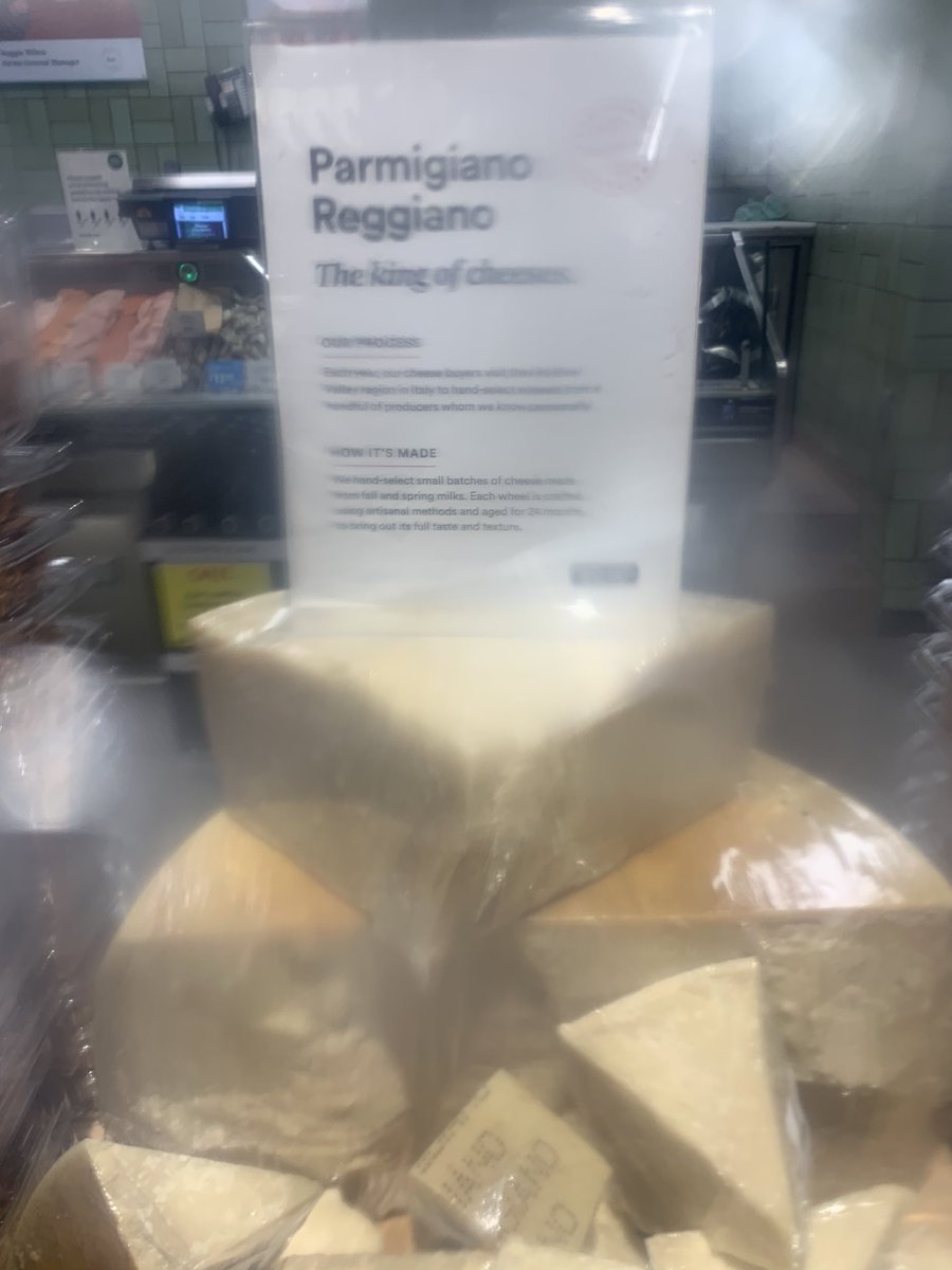 Big block of Parmigiano Reggiano at whole foods partially obscured by plastic cell phone bag