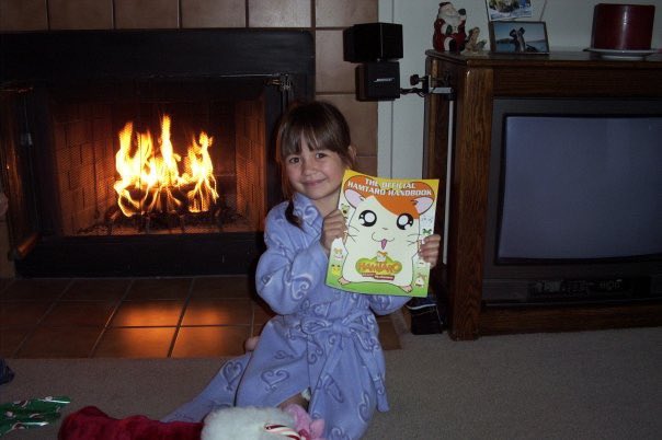 here is me on christmas morning as a child holding my hamtaro handbook i loved that show so much i used to stream it on our web tv