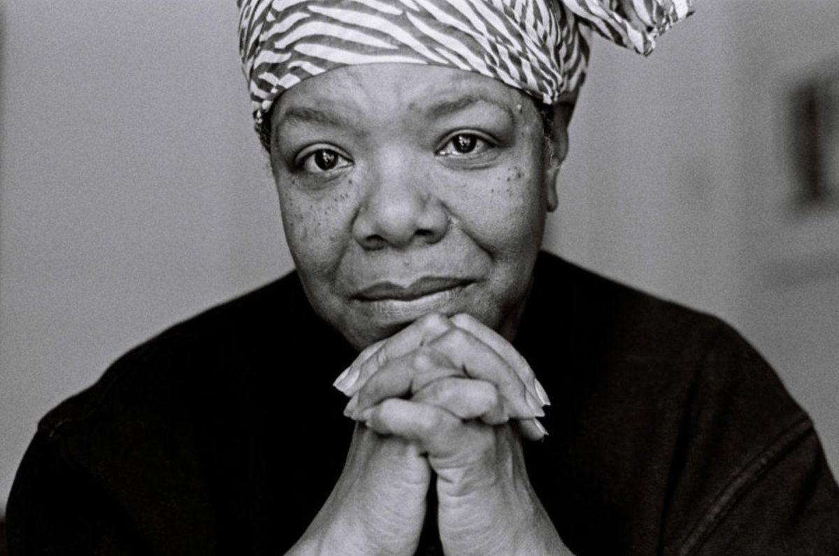 A photograph of Maya Angelou looking straight into the camera, with her hands clasped together underneath her chin.