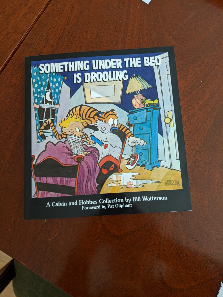 The book, Something Under The Bed Is Drooling, on a dark brown tabletop.