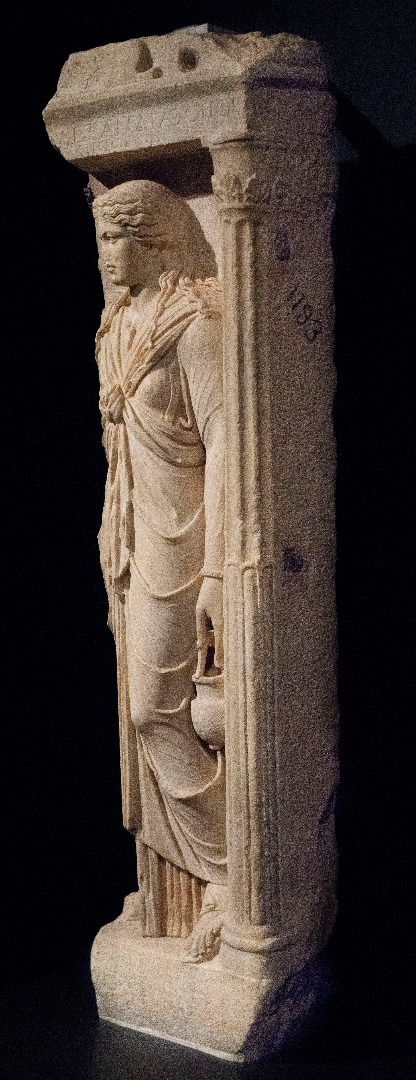 Marble Gravestone of Alexandra, Athenian priestess of Isis shown in the guise of the goddess. Her dress' central knot is characteristic of Isis cult devotees. Also her 2 ritual objects: situla [ritual bucket] & sistrum (rattle, now missing) AD 125-150, Kerameikos Cemetery, Athens