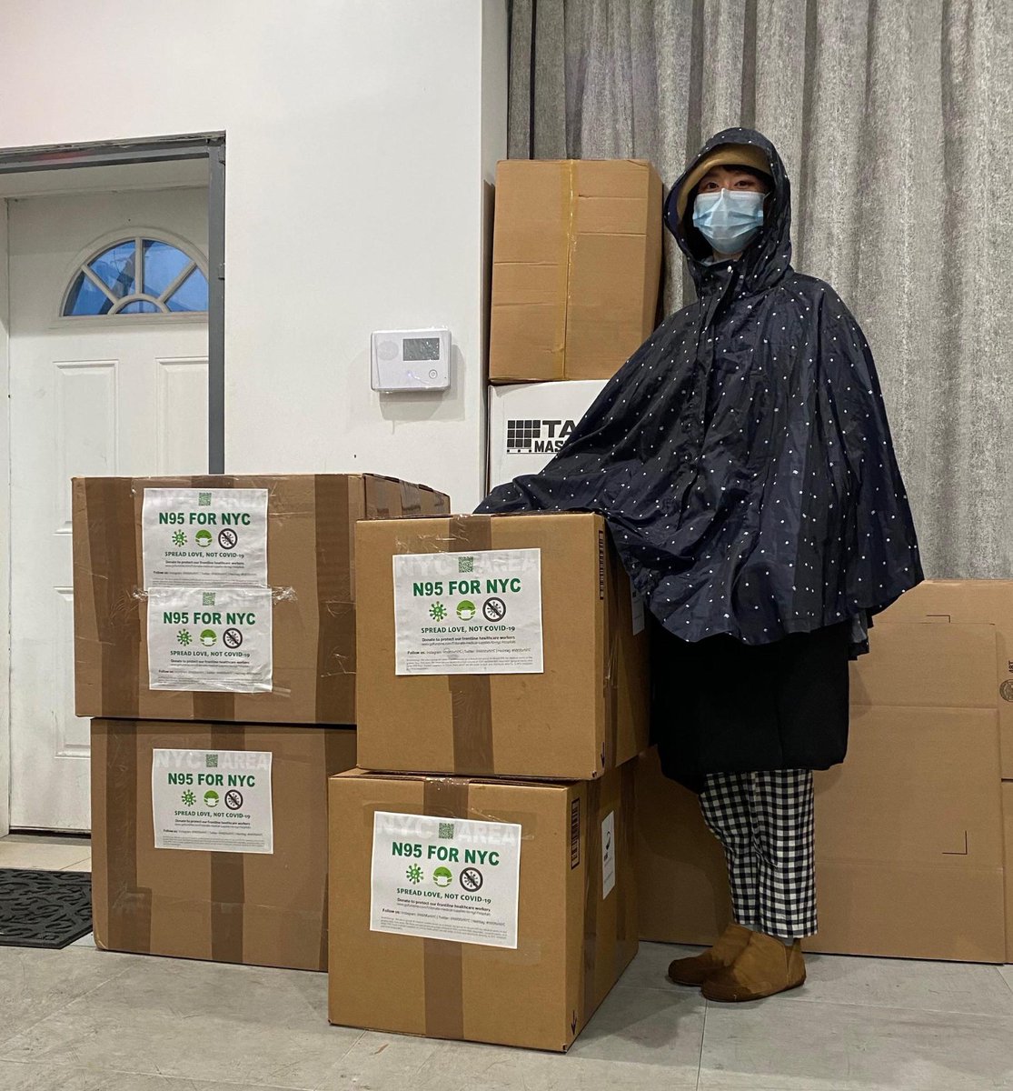 Echo He wearing a mask and poncho stands with boxes of medical coveralls which are being provided to doctors in Flushing, Queens