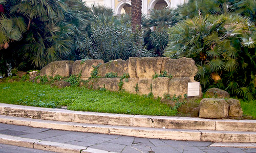 Frente a la iglesia, una pequeña y boscosa rotonda muestra restos de las murallas de Servio Tulio.