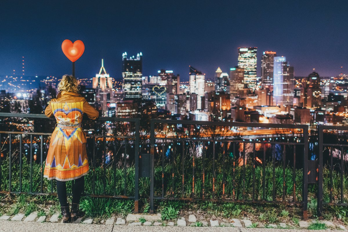 DaveDiCello's tweet photo. Jena, one of the organizers of #LovefromPgh, looks out over the #Pittsburgh skyline tonight with a heart light &amp; a colorful jacket, as the city is lit up in honor of those on the frontline of the pandemic. The lighting along Grandview was perfect, making for an incredible scene. https://t.co/AIalpcVCQU