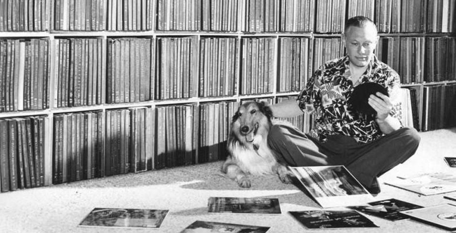 black and white photo of man looking through records with his dog
