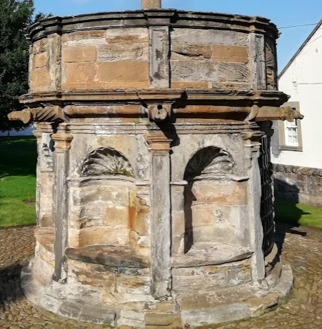 The base is an octagonal structure into which have been set 6 recesses, each scalloped to looks like a cockle-shell. Above these project nine cannon-shaped gargoyles and between them is a staircase leading up and a door to small chamber that *may* have acted as a tolbooth. (4/10)