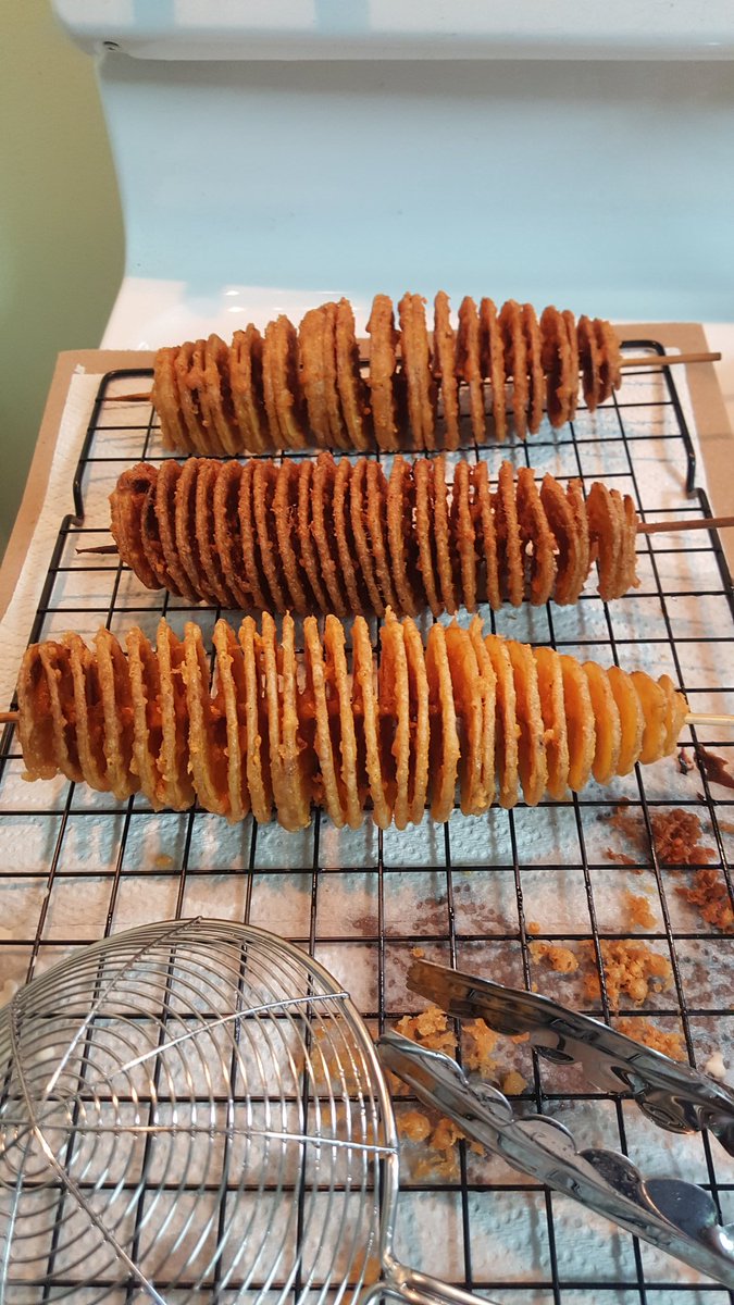 Photo of three battered and fried spiral cut potatoes on skewers