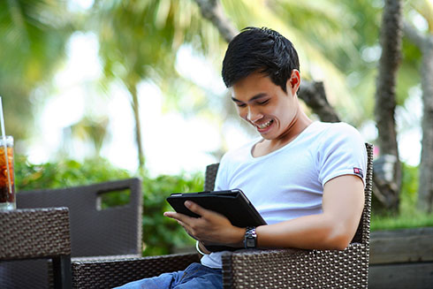 a man sitting at a patio table outside smiling while reading his tablet