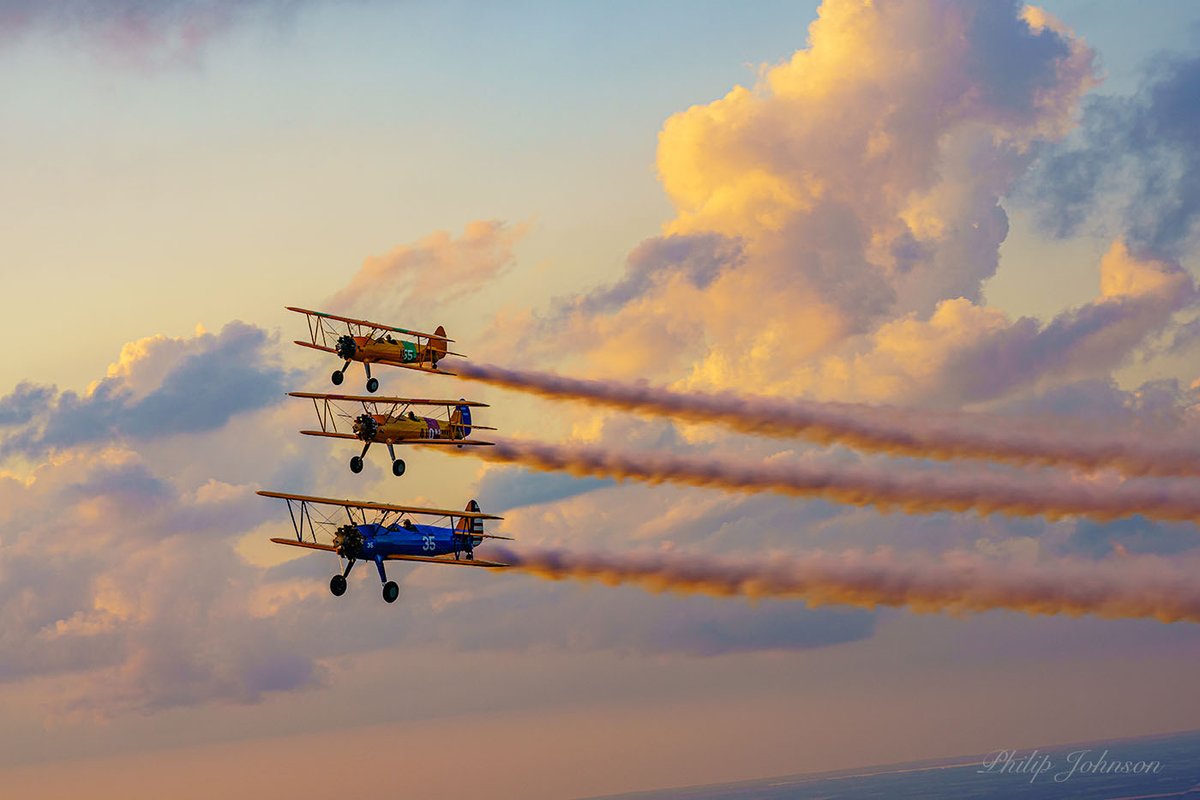 dartlrt's tweet photo. Here is a formation flight of 3 Stearman at sunset and smoke on.  Flying lead in his Army Stearman is Rod Hoctor, Navy colors with red strip is Ross Rodgers, and Navy Stearman with Green strip is Joe Beck. https://t.co/pQVFDMkGf1
