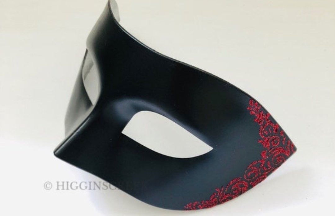 His hair is slicked all the way back, with only a few elegant pieces arranged to fall across his forehead.His eyes are covered by a black, strapless mask, of which swirling red accents are traveling down each side.