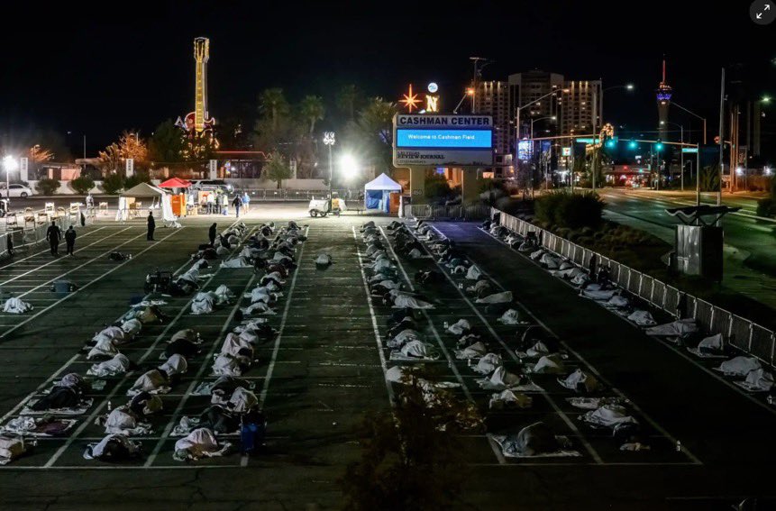 Dozens of homeless people sleeping in taped boxes on a concrete parking lot beneath $100M empty Las Vegas hotels.