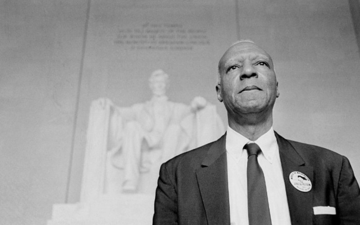 A photograph of A. Philip Randolph standing inside the Lincoln Memorial in Washington, DC. The statue of Lincoln is visible behind him as he stares straight out onto the National Mall.