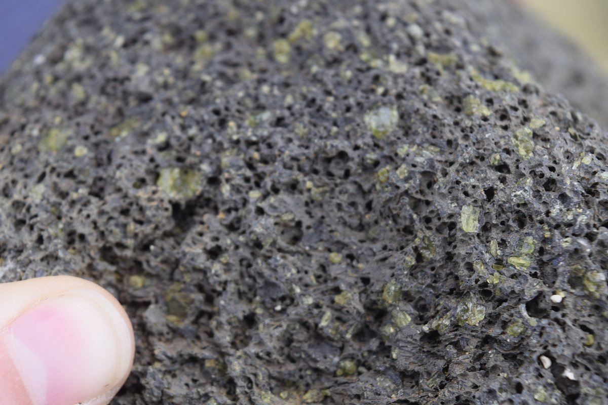 Il y a 49 000 ans, une éruption a éjecté plein de fragments de roches, qui sont encore visibles dans les falaises et qui contiennent beaucoup d'Olivine. Les vagues vont casser ces roches, et leurs cristaux d'Olivine, plus dense, vont rester coincé dans la baiePhoto : wikiwand