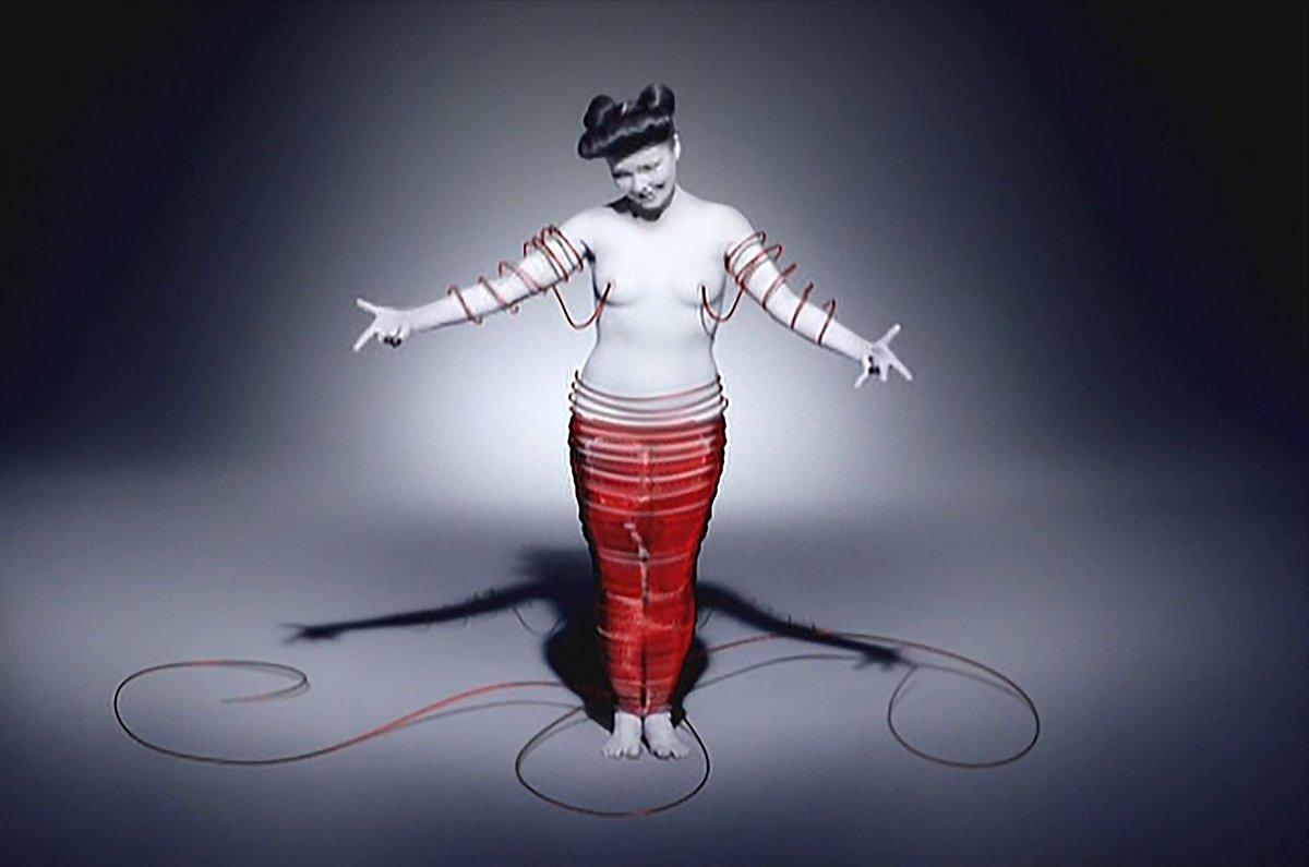 Cocoon (2002)The video begins with many apparently nude Björks singing. Throughout the video, red threads emerge from her nipples and circulate between her breasts and nose, finally enveloping her in a cocoon.