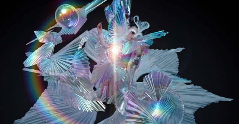 The Gate (2017)The video begins with Björk playing the flute on a cliff's edge, while several objects levitates. The 2nd part of the video portrays Björk passing a glowing orb to an "all-crystal being". A glow in her chest projects 3 other figures, that start dancing around her