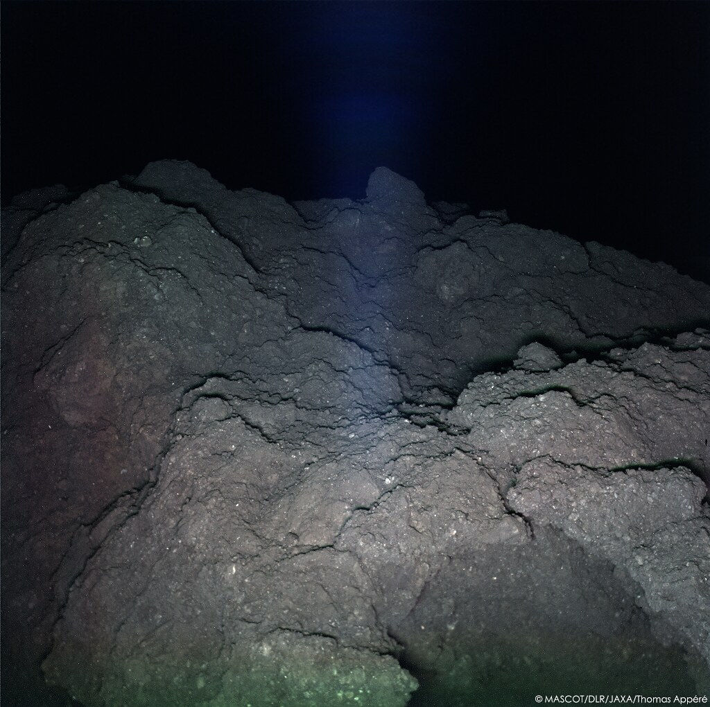 Pendant sa 2e nuit sur Ryugu, MASCOT illumine la surface avec 3 LEDs rouge, verte, bleue pour reconstituer cette image couleur du site d'atterrissage.Sur la dernière image, la saturation augmentée fait ressortir les couleurs : on distingue alors des inclusions rouges et bleues.