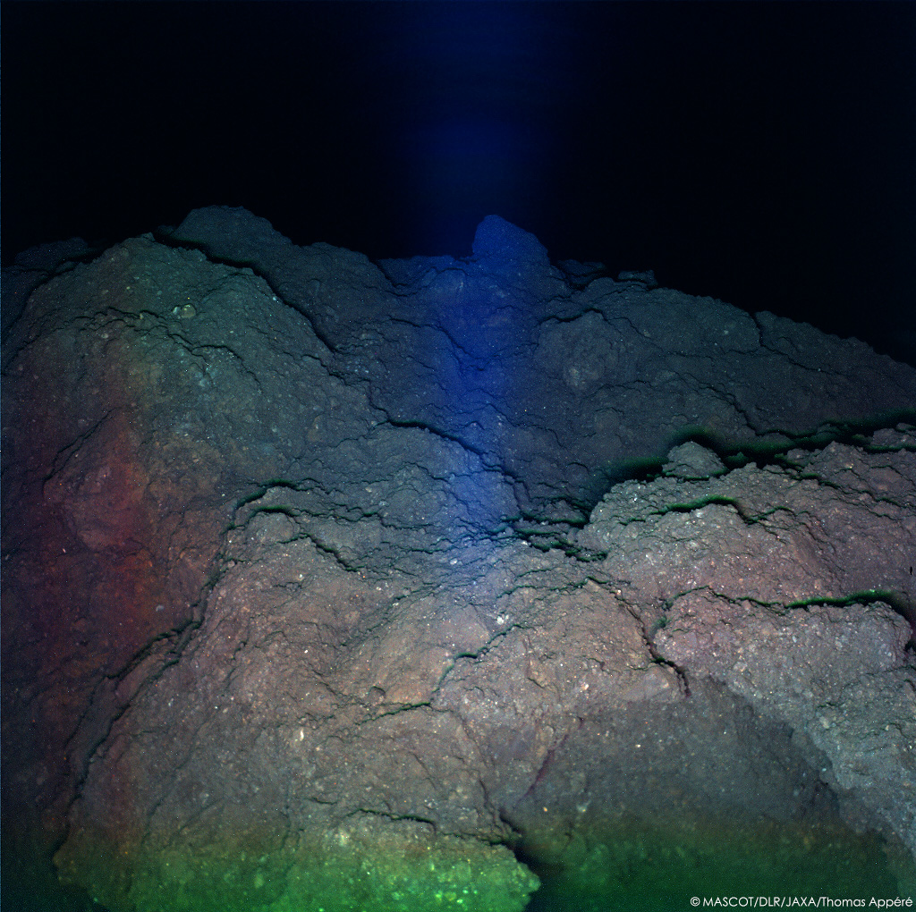 Pendant sa 2e nuit sur Ryugu, MASCOT illumine la surface avec 3 LEDs rouge, verte, bleue pour reconstituer cette image couleur du site d'atterrissage.Sur la dernière image, la saturation augmentée fait ressortir les couleurs : on distingue alors des inclusions rouges et bleues.