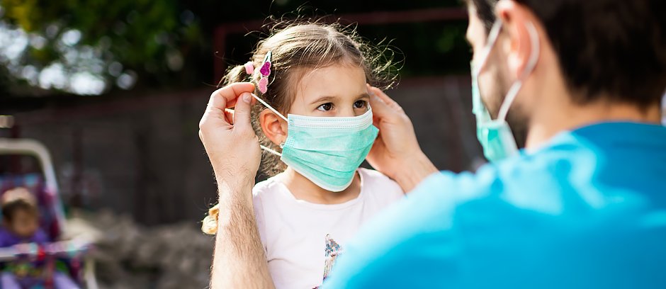 A man putting a surgical mask on a little girl