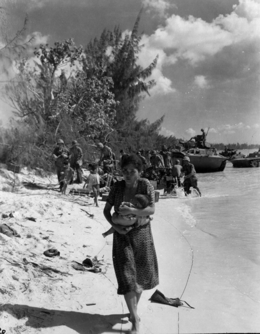  4: Une femme japonaise tenant un bébé évacue alors que des bateaux militaires américains sont vus en arrière-plan sur cette photo prise à Saipan en juin 1944.