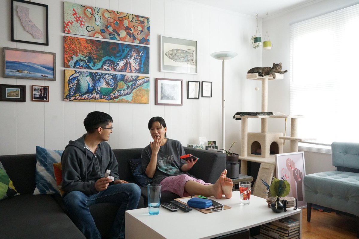 Me and Sam on the couch, my feet up on the coffee table looking at the box shocked with my had to my face still holding the Switch, Sam holding a small gray fuzzy box open and showing it to me, and both of us wearing grungy pajamas.